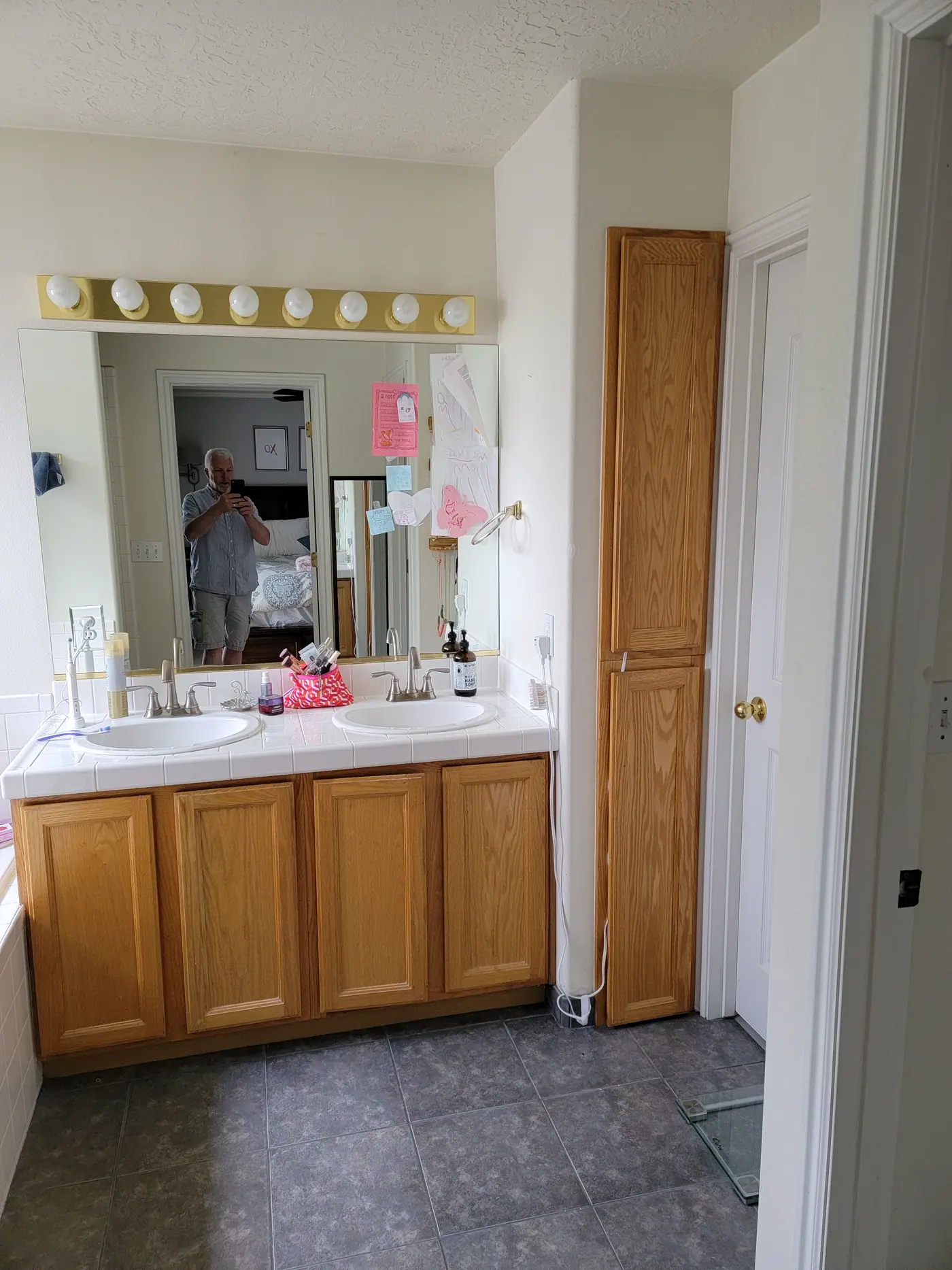 Before — oak double vanity with a Hollywood light bar and dated tile floor