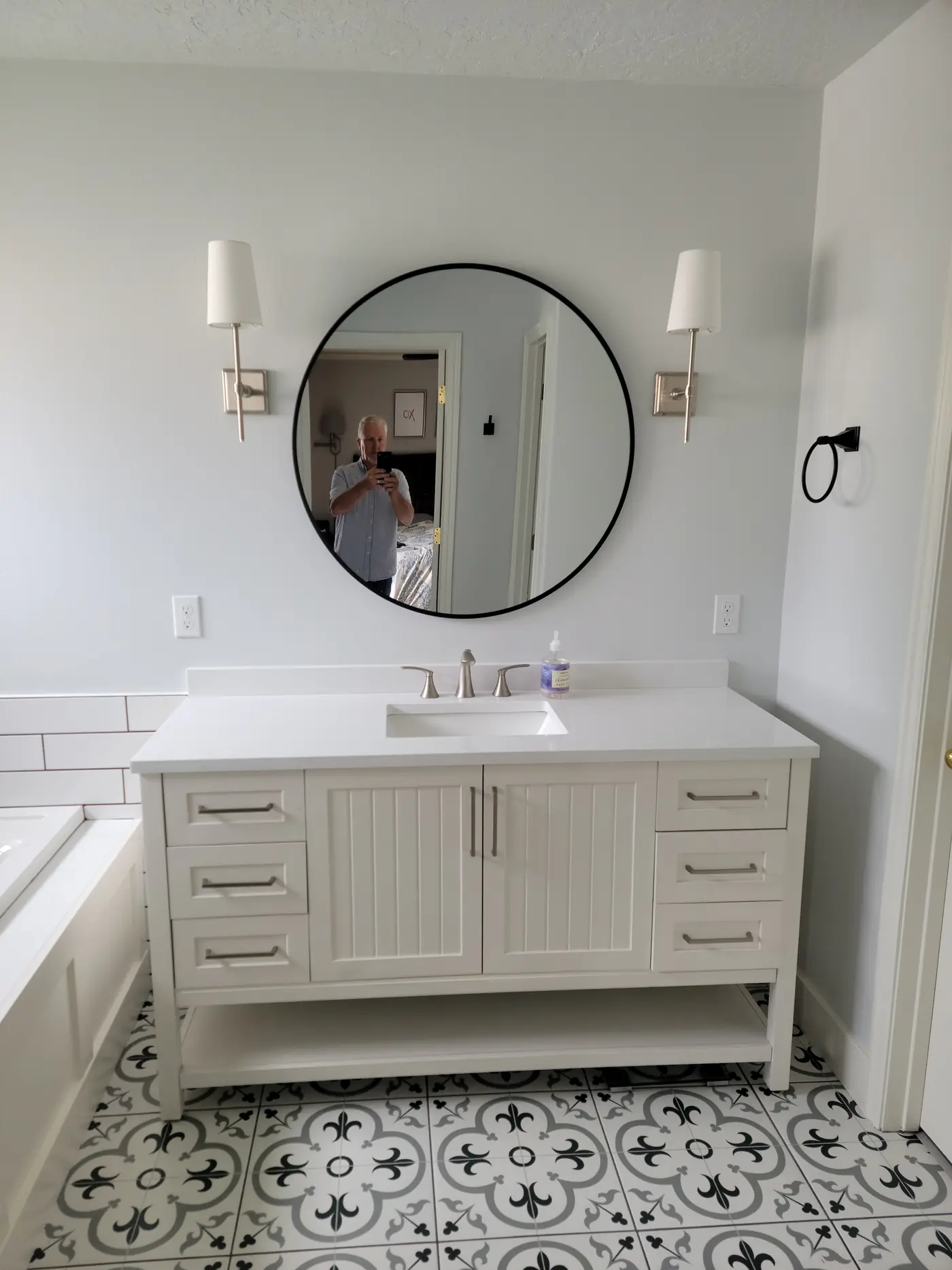 After — white shaker vanity, round mirror, wall sconces and patterned cement-look floor tile