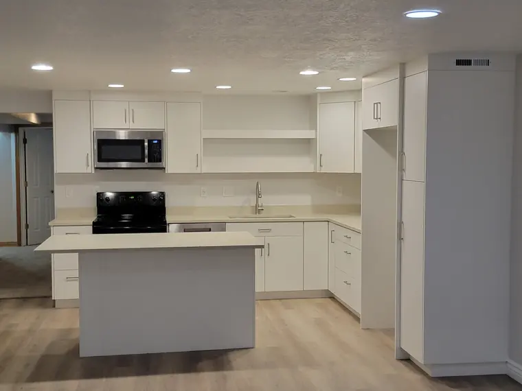 Finished basement kitchen with white cabinetry, quartz counters and an island