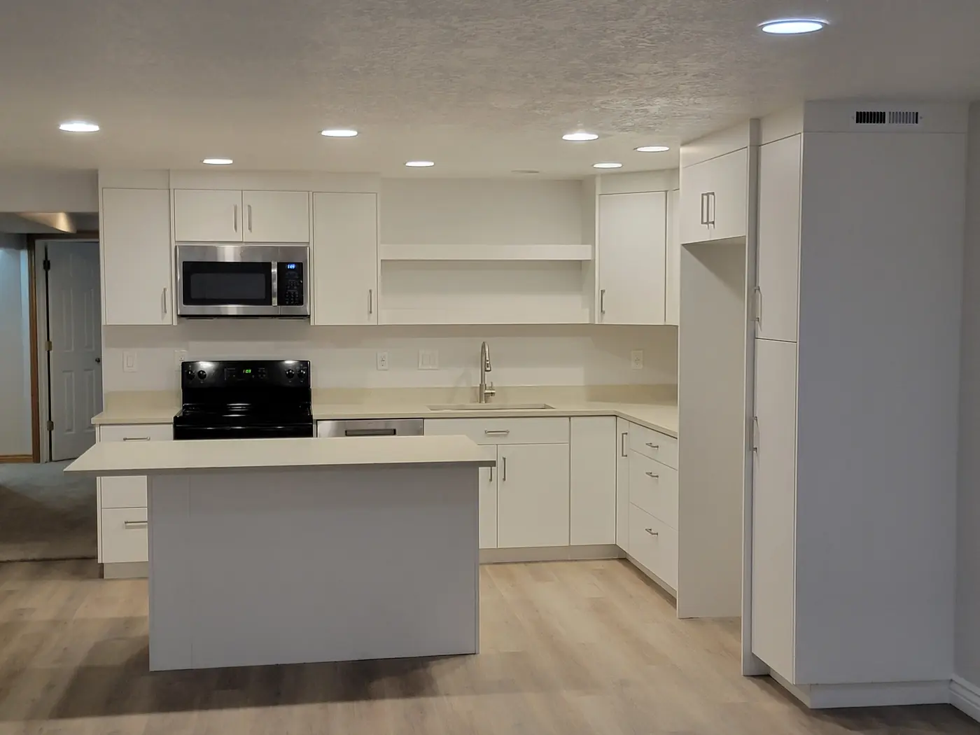 Finished basement kitchen — white cabinetry, quartz counters, island and plank flooring