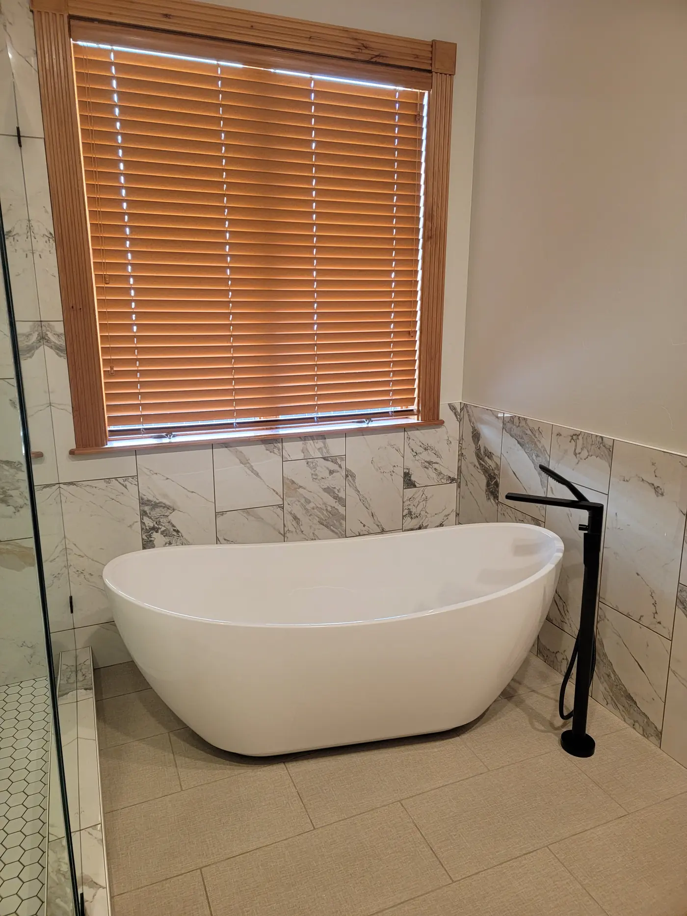 Finished primary bathroom — freestanding tub against marble-look tile, natural light from the window