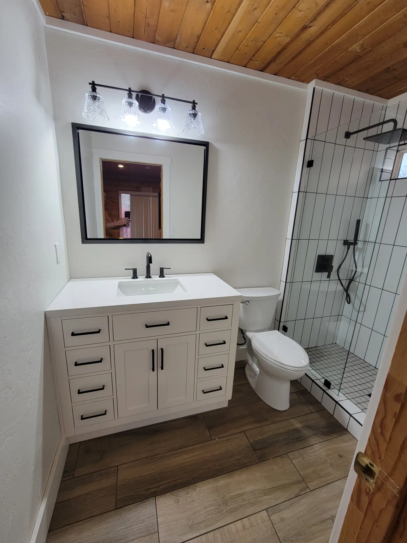 Finished guest bath — white vanity, black fixtures, walk-in shower, wood plank ceiling